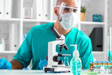 Maskeli ve yüz maskeli Afrikalı Amerikalı doktor masasında oturuyor.