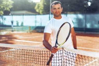 Tenis raketli Spoty adam kil kortunun yanında duruyor.