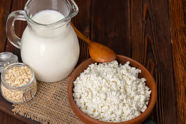 Glaskrug mit Milch und Schüssel mit Hüttenkäse auf Holztisch — Stockfoto