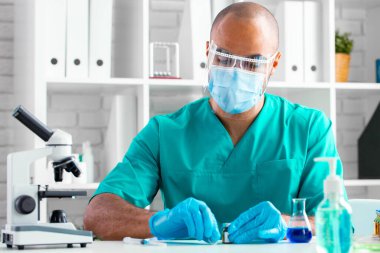 Afro-Amerikalı doktor masada oturuyor ve bir ilaç enjekte etmeye hazırlanıyor.