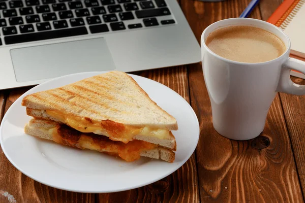 Triangle sandwich on wooden office table with laptop and coffee cup — Stock Photo, Image