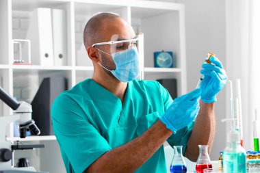 Afro-Amerikalı doktor masada oturuyor ve bir ilaç enjekte etmeye hazırlanıyor.