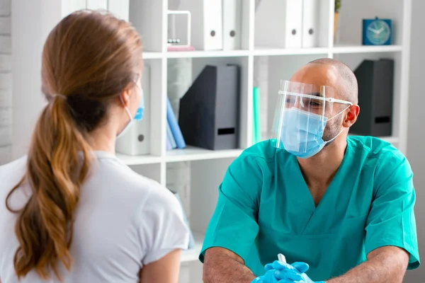 Arzt mit Gesichtsmaske spricht Patientin in Klinik an — Stockfoto