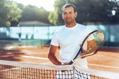 Tenis raketli Spoty adam kil kortunun yanında duruyor.