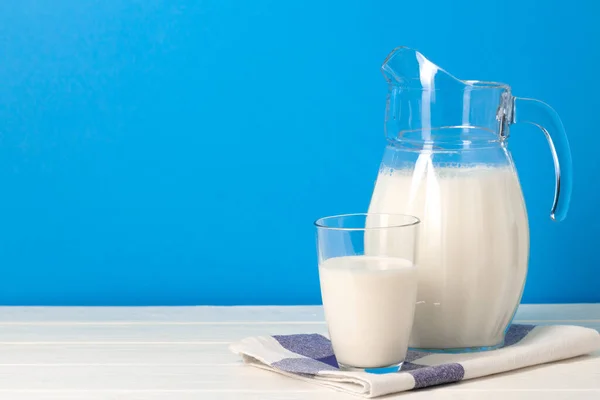 Mavi arka plana karşı bardak ve sürahi süt — Stok fotoğraf