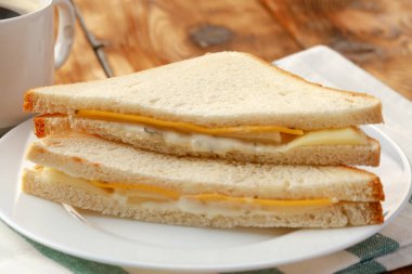 Tahta masadaki peçetede tost sandviçi ve bir fincan kahve.