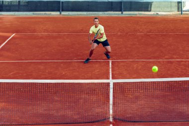Genç yakışıklı adam tenis kortunda tenis oynuyor.