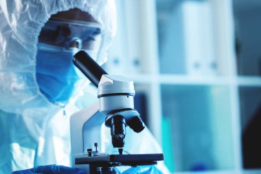 Mikroskop altında koruyucu elbise giyen bir tıp çalışanı.