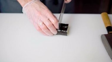 Erkek aşçı elleri restoranın mutfağında maki suşi rulosunu kesiyor.