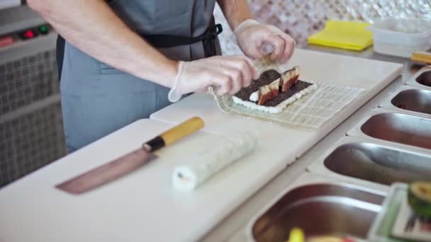 Manos masculinas en guantes cocinando rollos de sushi en una cocina de restaurante de cerca — Vídeos de Stock