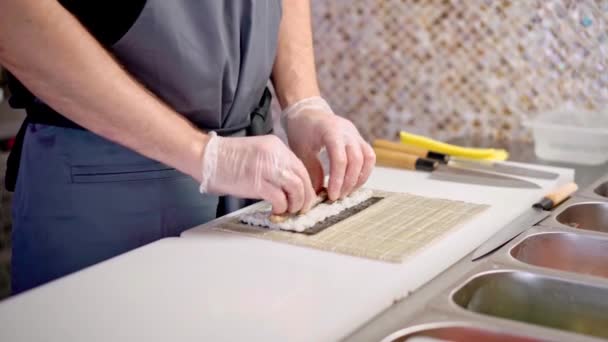 Manos masculinas en guantes cocinando rollos de sushi en una cocina de restaurante de cerca — Vídeos de Stock