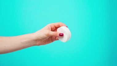 Mavi arka planda kozmetik pamuk diskleri tutan kadın.