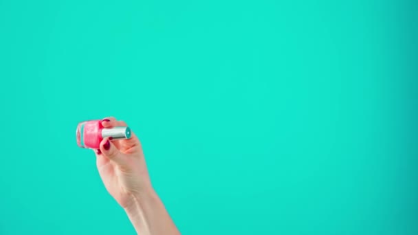 Žena ruka drží láhev lak na nehty proti modrému pozadí — Stock video
