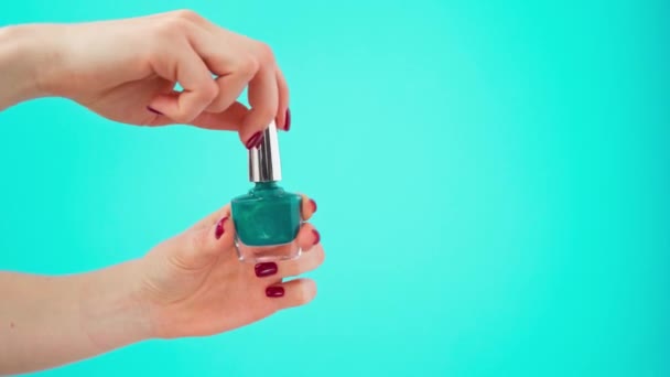 Botella de mano femenina de esmalte de uñas sobre fondo azul — Vídeo de stock