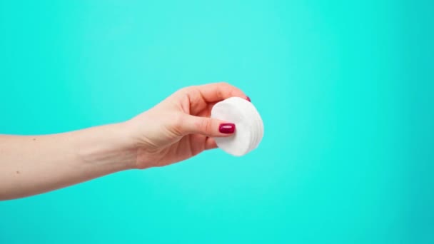 Main féminine tenant des disques de coton cosmétique sur fond bleu — Video