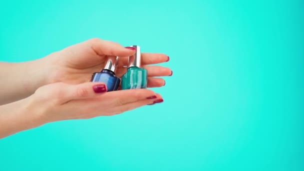 Manos femeninas sosteniendo dos botellas de esmalte de uñas sobre fondo azul — Vídeo de stock