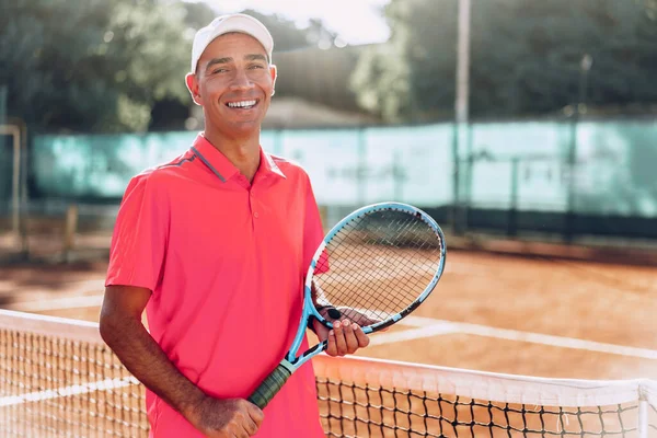 Middle-aged man tennis player with racket standing on court near net