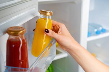 Bir kadın buzdolabından portakal suyu kavanozunu alıyor.