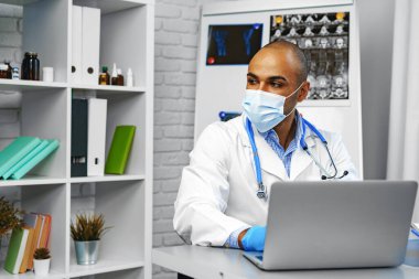 Karışık ırk erkek doktoru hastanede çalışma masasında oturuyor.