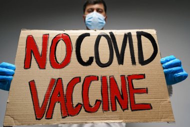 Doktor elinde COVID aşı metni olmayan protesto pankartı tutuyor.