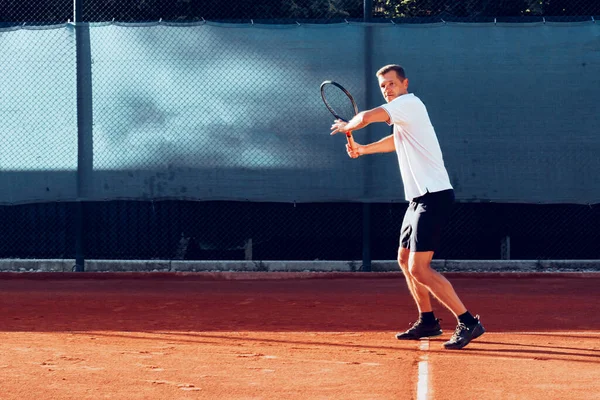 Junger Mann spielt morgens Tennis im Freien auf Tennisplatz — Stockfoto