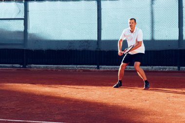 Genç adam sabahları tenis kortunda tenis oynar.