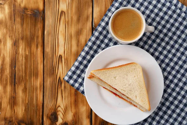 Бутерброд с тостом и чашка кофе на салфетке на деревянном столе — стоковое фото
