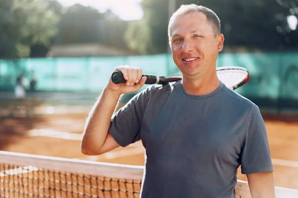 Middle-aged man tennis player with racket standing on court near net