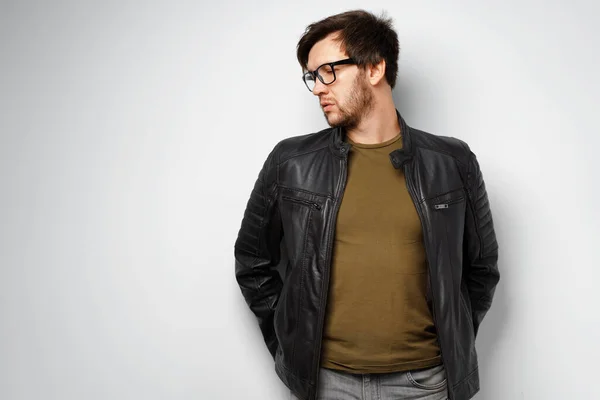 Portrait of a young man in glasses wearing black leather jacket on grey background — Stock Photo, Image