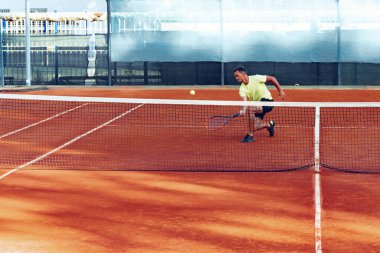 Genç yakışıklı adam tenis kortunda tenis oynuyor.
