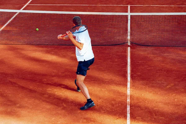 Вид сзади на человека, играющего в теннис на теннисном корте — стоковое фото