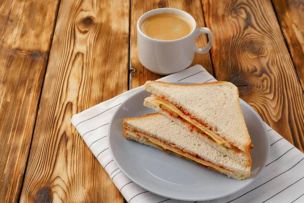 Tahta masadaki peçetede tost sandviçi ve bir fincan kahve.