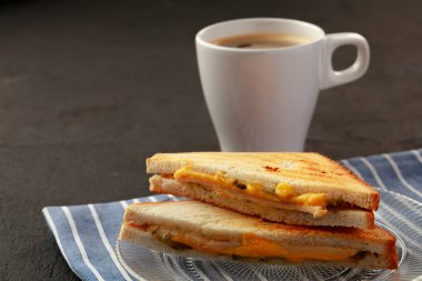Tahta masadaki peçetede tost sandviçi ve bir fincan kahve.