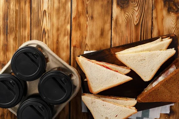 Čtyři šálky kávy a čtyři sendviče na dřevěném stole — Stock fotografie