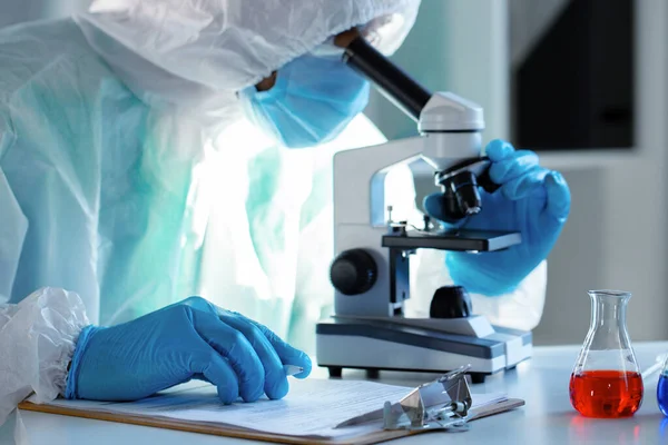Медичний працівник у захисному сукні дивиться в мікроскоп — стокове фото