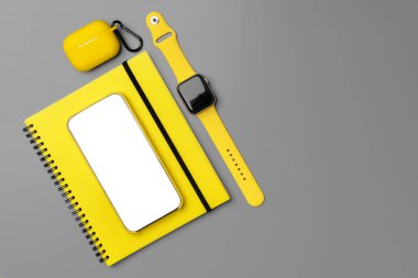 Akıllı telefon, akıllı seğirme ve gri arka planda kulaklık olan sarı not defteri.