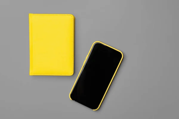 Gele notitieblok en smartphone op grijze achtergrond — Stockfoto