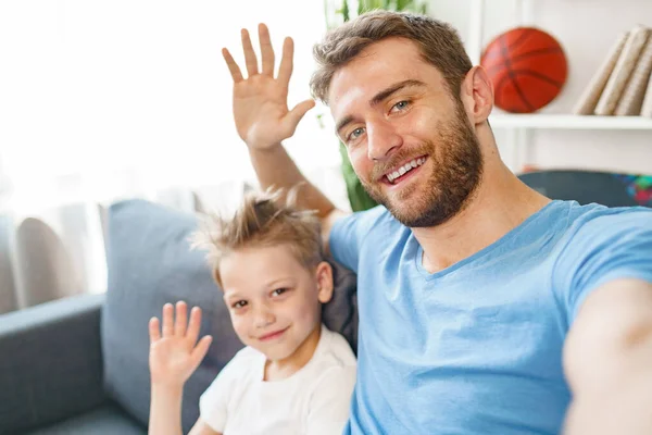 아버지 와아들은 소파에 앉아 카메라 앞에서 손을 흔들고 있다 — 스톡 사진