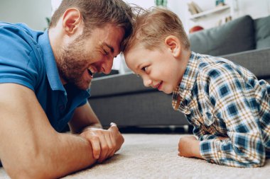 Baba ve oğul evde halıda birlikte oynuyorlar.