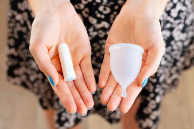 Adet bardağı ve tıbbi tampon tutan kadın elleri.
