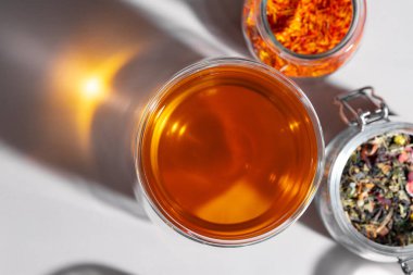 Beyaz masada bir bardak çay ve kuru çay yaprağı.