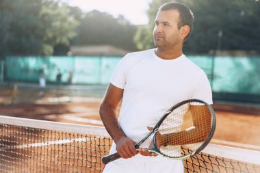 Tenis raketli Spoty adam kil kortunun yanında duruyor.