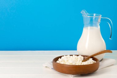 Bir sürahi süt ve ahşap masada bir kase süzme peynir.