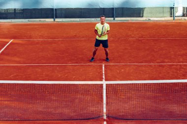 Genç yakışıklı adam tenis kortunda tenis oynuyor.
