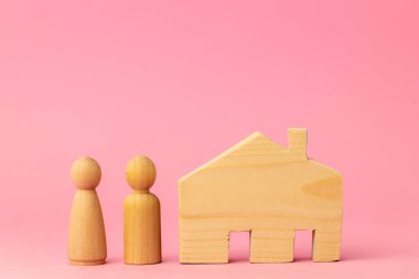 Ahşap ev minyatürü ve pembe arka planda oyuncak insanlar.