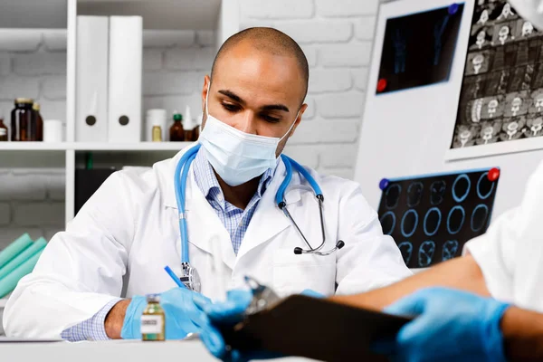 Karışık ırk erkek doktoru hastanede çalışma masasında oturuyor. — Stok fotoğraf