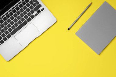 Sarı arka planda dizüstü bilgisayar, not defteri ve kalem.