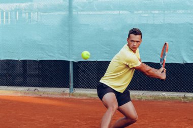 Genç yakışıklı adam tenis kortunda tenis oynuyor.