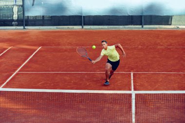 Genç yakışıklı adam tenis kortunda tenis oynuyor.