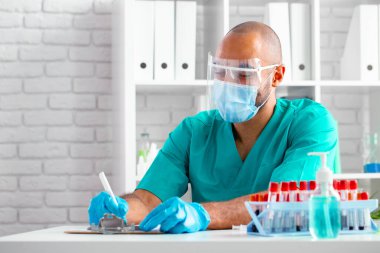 Afro-Amerikan doktor masasında otururken not alıyor.